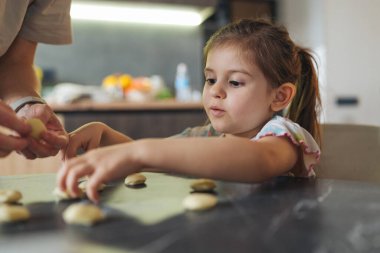 Bebekler hamuru tezgahın üzerinde ebeveyn rehberliği ile şekillendiriyor, elle hareket becerilerini öğreniyor ve nazikçe teşvik ediyor.