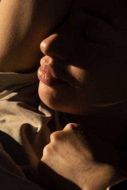 Yakından portre dudaklar gölgede yumuşak sıcak ışık tende, gözler kapalı, kadın şair duraksıyor, yumruğunu sıkmış.