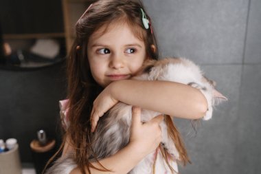 Beyaz kız kediyi aynayla kucaklıyor, yakından portre çekiyor narin bakışları ve yumuşak kürkü gri fayansların arkasında sıcak tutuyor.