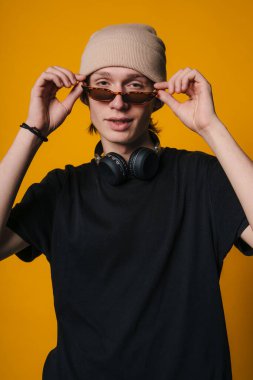 Beyaz adamın güneş gözlüğünü kulaklıkla, bereyle ve sarı arkaplanla ayarlaması etkileyici bir etki yaratıyor, DJ.