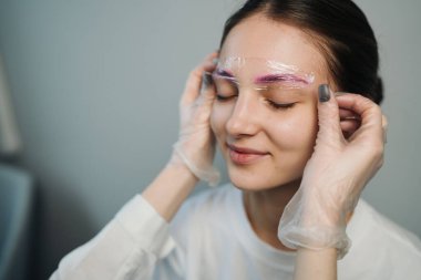 Kaş haritalama sırasında gülümseyen beyaz kadın, yapışkan bantlarla estetik danışmanlığı, ayarlayan eldivenli eller.