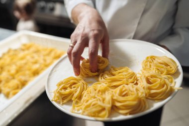 Beyaz tabakta taze makarna, aşçı el yapımı tagliatelle yuvaları meşgul mutfakta, tepside bulanık yuvalar.