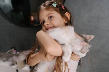 Çocuk kediye sıkıca sarılıyor gözleri kapalı, yumuşak bir kucaklama ve yumuşak bir kürk, içten bir bağ ve koruyucu tutuş, huzurlu bir sessizlik anı.