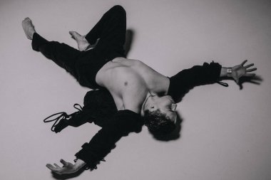 Monokrom stüdyosunda yakalanan yaslanmış bir sanatçı. Tişörtsüz model, kollarını açmış, duygularını askıya almış ve kıvrımlı yatar.