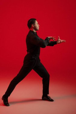 Cesur kırmızı arka planda erkek oyuncu, geniş duruş öne uzanıyor, dengeli uzatma, teatral ifade, özel dikim siyah giysi,