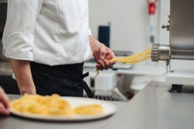 Makarna makinesi makineden taze spagetti, paslanmaz dışkı ve hamur, öndeki yuvaların tabağı, endüstriyel mutfak.