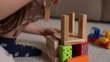 Kafkasyalı kız uzun tahta kuleyi dengeliyor, hassas eller dikey sütunlara, yumuşak halı tabanına, oyuncak trene yerleştirilmiş.