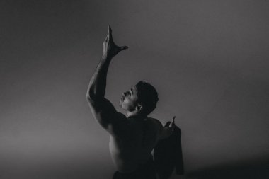 Siluetli erkek, kolunu kaldırmış, ceketi omzunun üzerine sarılı, yüksek kontrastlı tek renkli ışıklandırma, güçlü dış hatlar, kalın hatlar.