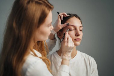 Danışmanlık sırasında müşteri kemerlerini şekillendiren sanatçı, araçlar ve ayna kullanan stilist, sıcak iç aydınlatma,