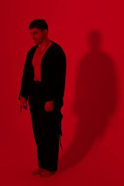 Kırmızı sette bir adamın dramatik kırmızı portresi, yalınayak aşağı bakan bakışlı, duvarda yalın gölge, teatral ışıklandırma, ham