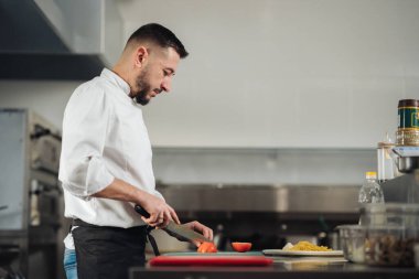 Şef istasyonda dolma biber dilimliyor, yoğun konsantrasyon ve kırmızı kesme tahtasında keskin bıçak tekniği, paslanmaz aralık.