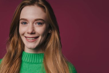 Kırmızı saçlı, gülümseyen kadın, Burgundy 'ye karşı yeşil kazak giyen, kendine güvenen modelin stüdyo fotoğrafı.