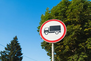 Siyah kargo kamyonu olan kırmızı ve beyaz trafik işaretleri arka planda ağaçlı ve mavi gökyüzü olan kamyonlara giriş olmadığını gösteriyor.