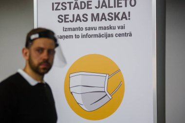 RIGA, LATVIA. 23 Ekim 2020. Seçici odak fotoğrafı. Gösteri merkezindeki pankartta koruyucu maske sembolü.