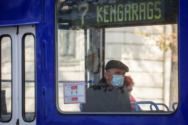 RIGA, LATVIA. 8 Ekim 2020. Seçici odak fotoğrafı. Tramvayda yüz koruyucu maske takan biri..