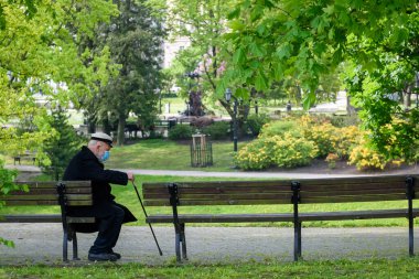 RIGA, LATVIA. 28 Mayıs 2020. Yüzü maskeli yaşlı bir adam parkta bankta oturuyor..