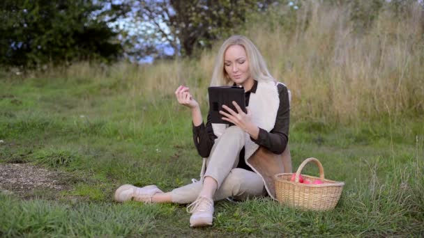 Молодая женщина держит в одной руке яблоко, в другой руке планшет — стоковое видео