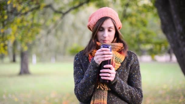 Mooie jonge vrouw wordt geopend een thermocup en drinken zeer hete thee uit in de herfst park. — Stockvideo