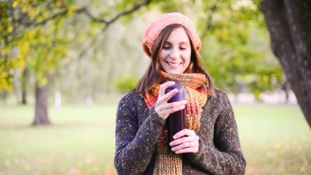 Beautiful young woman opens a thermocup and drink very hot tea from it in autumn park. — Stock Video