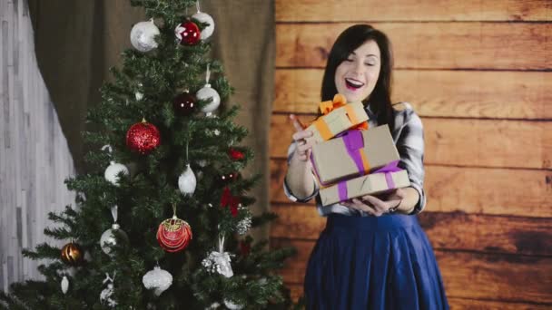 Hermosa joven se para cerca de un árbol de Navidad, considerando un regalo y luego presenta un regalo — Vídeos de Stock