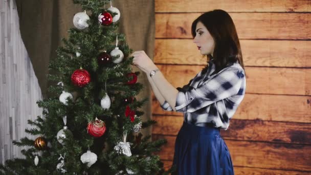 Beautiful young woman decorates a Christmas tree at home — Stock Video