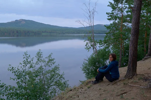 山に対する湖畔に座っている女性の後ろ姿 — ストック写真