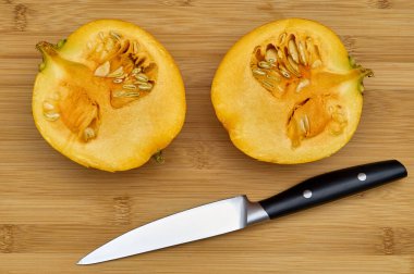 Mutfak bıçağının yanındaki tahta kesme tahtasının üzerinde balkabağının iki yarısı görünüyor.