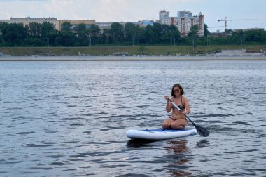 Şehrin altında kumsalda kürek çeken mutlu güzel bir kadın. Yaz, tatil, yemek masası ya da sörf, seyahat, yaşam tarzı konsepti.