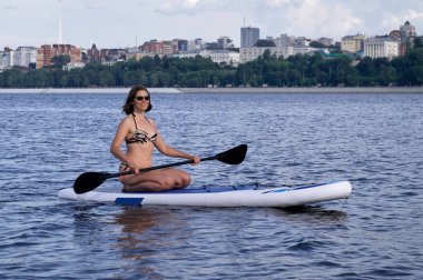 Şehrin altında kumsalda kürek çeken mutlu güzel bir kadın. Yaz, tatil, yemek masası ya da sörf, seyahat, yaşam tarzı konsepti.