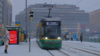 Helsinki, Finlandiya - 12 Ocak 2021: Şiddetli kar fırtınası sırasında Merkez Tren İstasyonu yakınında tramvay durağı. İnsanlar tramvayı bekliyor. Tramvay istasyondan ayrılıyor..