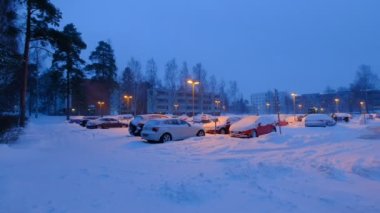 Espoo, Finlandiya - 13 Ocak 2021: Şiddetli kar fırtınası sırasında açık hava parkında bir sürü kar kaplı araba. Traktör kar fırtınasından sonra caddeyi temizliyor..