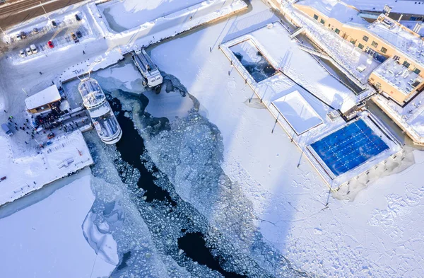 Aerial view of the outdoor heating pool Allas Sea Pool and the Suomenlinna ferry dock on a sunny winter day. Modern nordic wooden architecture. Helsinki, Finland