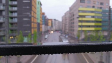 Avrupa şehrinin modern mahallesinin caddesinin bulanık görüntüsü. Tramvay caddede ilerliyor. Ön planda, yağmur sırasında köprünün ıslak siyah çelik çiti. Helsinki, Finlandiya.