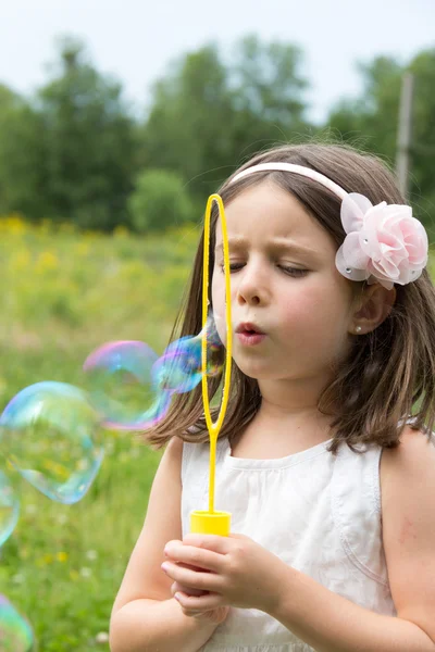 Liten flicka i vit klänning blåser bubblor på park — Stockfoto