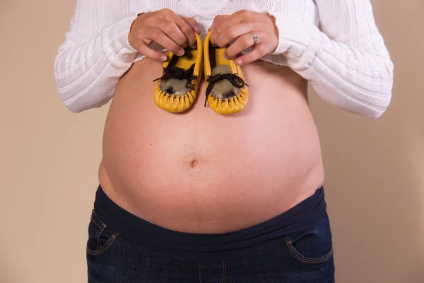 Menina grávida com sapatos de bebê em sua barriga exposta — Fotografia de Stock