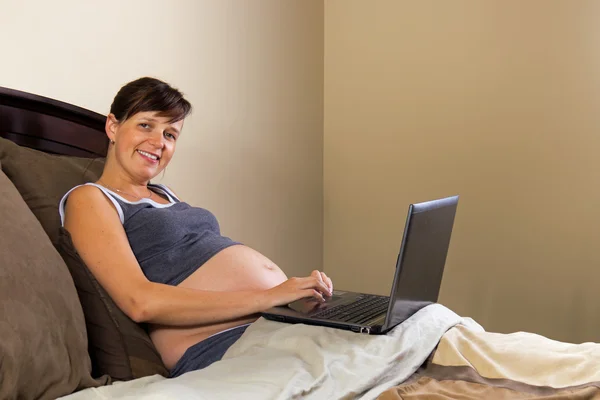 Femme enceinte travaillant avec un ordinateur portable sur son lit — Photo