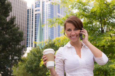 Kahve akıllı telefon kullanarak kentsel Park ile gülümseyen kadın