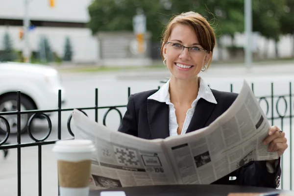 Smiling business woman reads newspaper at outdoor coffee shop — Stock Photo, Image