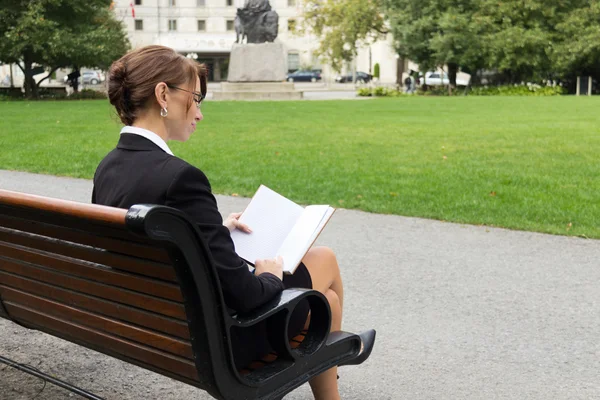 Business woman reads while sitting on park bench — Stock Photo, Image