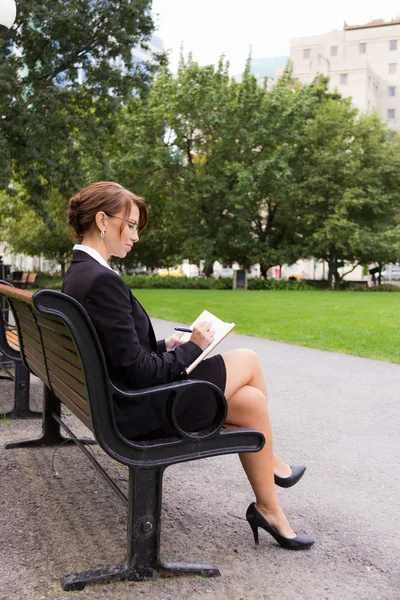 Zakenvrouw zit op bankje voor parken en schrijft notities — Stockfoto