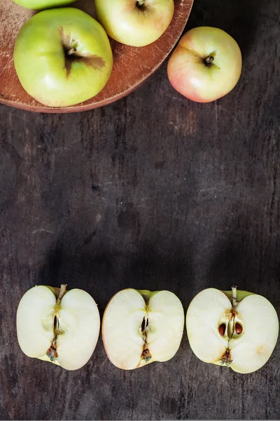 Tres manzanas en una tabla de tallar y tres mitades de manzanas en una mesa de madera — Foto de Stock