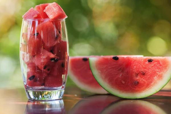 Wassermelonenstücke in einem Glas und Wassermelonenscheiben auf einem Tisch liegend — Stockfoto