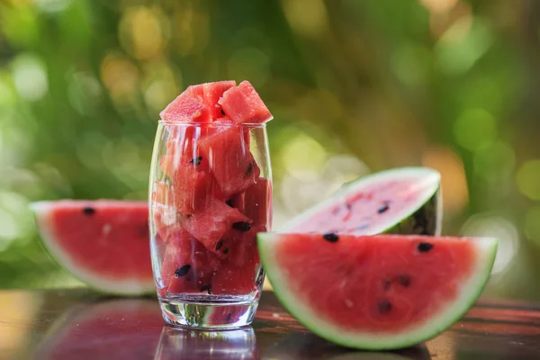 Wassermelonenstücke in einem Glas und Wassermelonenscheiben auf einem Tisch liegend — Stockfoto