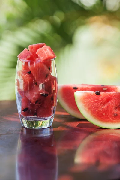 Trozos de sandía en un vaso y rodajas de sandía tumbadas en una ta — Foto de Stock