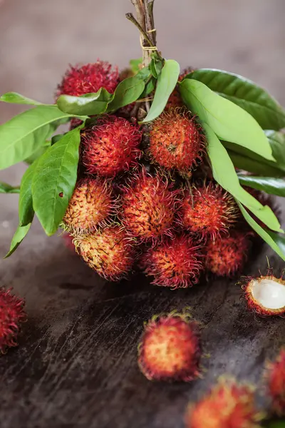 A bunch of rambutans and leaves on a brown wooden table — Stock Photo, Image