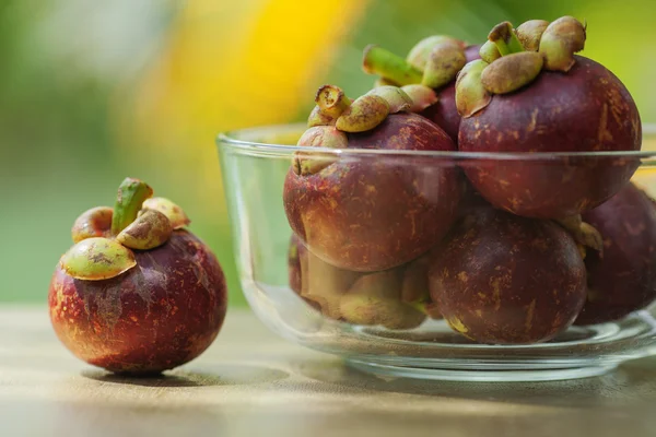 Mangostanes en un tazón de vidrio y uno sobre la mesa — Foto de Stock