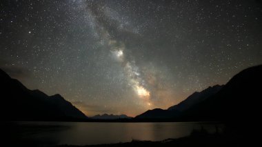 Samanyolu Galaksisi 'nin canlı şeridi karanlık ve uzak bir dağ manzarası boyunca uzanan gece gökyüzüne hakim..