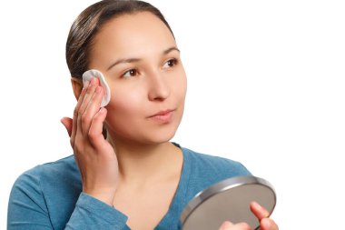 Genç bir kadın yüzünü losyonla pamukla siliyor, aynaya bakıyor ve gülümsüyor. Beyaz arkaplanda izole.