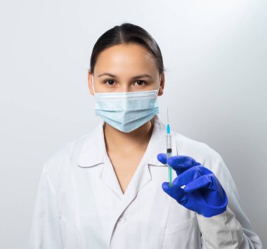 Beyaz arka planda elinde şırıngayla koruyucu maskeli kadın doktor..