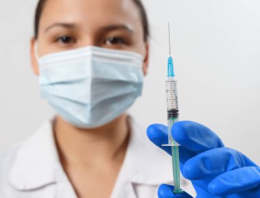 Eldivenli bir doktor ve şırıngalı koruyucu bir maske. Coronavirus covid-19 'a karşı aşı